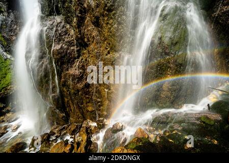 Regenbogen am Dalfaz Wasserfall unterhalb des Dalfaz Klettersteigs am Achensee im Rofangebirge. Wasser fällt in die Felswand und bildet einen wunderbaren kleinen doppelten Regenbogen in der Sonne. Stockfoto