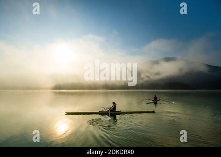 Kajakfahrer oder Rennfahrer genießen eine Fahrt auf dem Sylvensteinspeicher am frühen Morgen bei Sonnenaufgang, bei Nebel und leichter Stimmung. Stockfoto