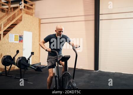 Fit Mann in Sportbekleidung Reiten auf einem stationären Fahrrad während Eine Trainingseinheit im Fitnessstudio Stockfoto