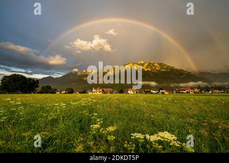 regenbogen über der bayerischen Stadt Krün in den Alpen. Im Hintergrund die Schöttelspitze und Soierngruppe im Karwendelvorland, beleuchtet von der Abendsonne. Stockfoto