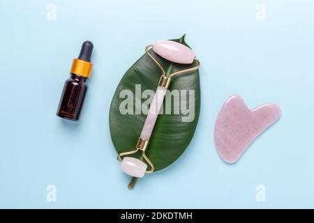 Kosmetikflaschen, Gesichtsserum, Gesichtsmassageroller und Gua Sha Massagegerät auf blauem Hintergrund. Anti-Age-, Lifting- und Toning-Behandlung zu Hause - Bild Stockfoto