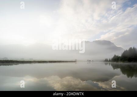 Herbststimmung an einem kleinen See in den bayerischen Alpen, im Hintergrund das Karwendelgebirge, eine kleine Halbinsel im Nebel und die Spiegelung im Wasser. Die neblige Atmosphäre mit den zerklüfteten Bergen hat eine fast mystische Wirkung. Stockfoto