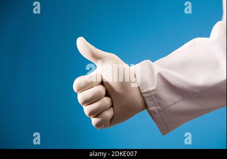 Hand des Arztes tut ok Symbol, mit chirurgischen Handschuh und blauen Hintergrund Stockfoto