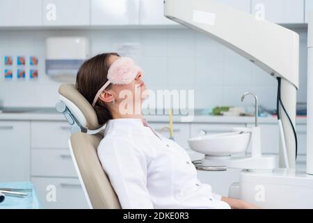 Ein Arzt, der mit einer Schlafmaske im Zahnstuhl ein Nickerchen macht. Stockfoto