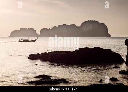 Kleine Inseln vor Phi Phi Inseln im Abendlicht. Ein Longtail-Boot fährt nach Bamboo Island. Stockfoto