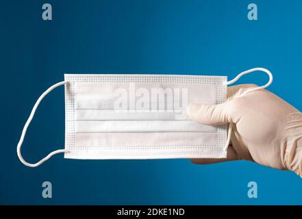 Gesichtsmaske in Arzthand mit OP-Handschuh und blauem Hintergrund. Stockfoto