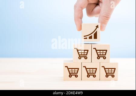 Verkauf Volumensteigerung machen Geschäft wachsen Konzept. Hand des Geschäftsmannes baut eine Pyramide aus Holzwürfeln mit Verkauf Ikonen. cube mit Symbol Grafik und shoppi Stockfoto