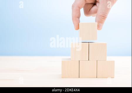 Hand legt baut eine Pyramide aus leeren Holzwürfeln. Ein würfelförmiger Holzblock in Pyramidenform ohne Grafiken für Business Design Concept gestapelt. Stockfoto