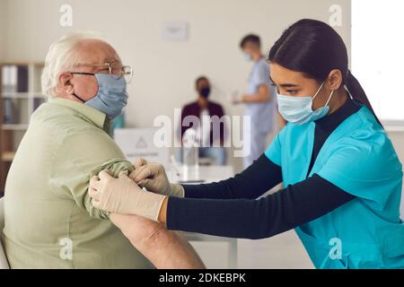 Frau Arzt Krankenschwester in medizinischen Uniform und Schutzmaske machen Impfung älterer Mann Stockfoto