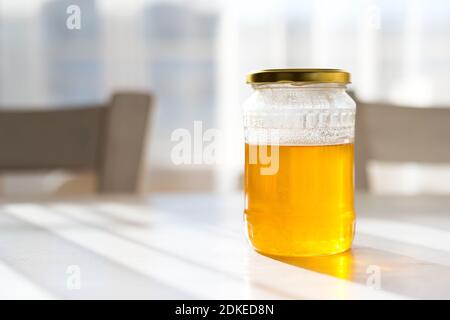 Ein Glas Honig auf einer alten alten weißen Küche Tisch gegen das Sonnenlicht aus dem Fenster - selektiver Fokus Stockfoto