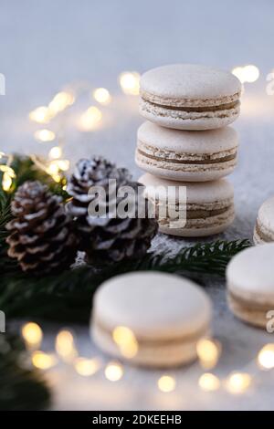 Vanilla macarons stacked on a white table, winterly decorated with fir branches and pine cones, a sring of light shines in the background Stock Photo