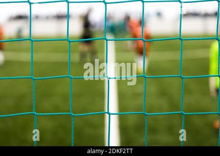 Fußballplatz durch Tornetz. Grünes Fußball-Tornetz. Verschwommenes Fußball stadum im Hintergrund Stockfoto