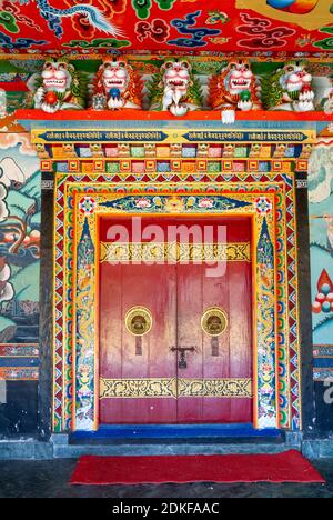 Bunt dekoriert, mit einem kunstvoll gefertigten und verzierten Türknöpfe Eingang zu einem Tempel des Rumtek buddhistischen Klosters (Sikkim, Indien), bemalte Wände Stockfoto