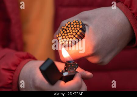 Man in Red Jacked Lighting Up Many Small Black Firecrackers in his Hand Using Gasoline Lighter. Guy Getting Ready for New Year Fun with Fireworks or Pyrotechnic Products Stock Photo