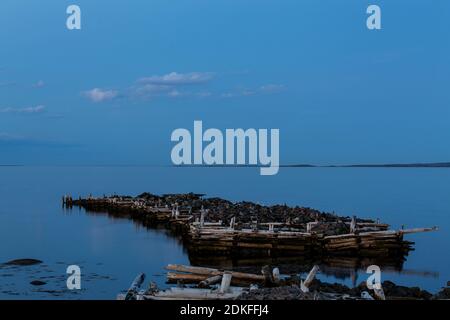 Alte zerstörte Pier im Meer an einem bewölkten, bösen Vollmond am späten Abend, Weißes Meer, Russland Stockfoto