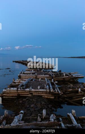 Alte zerstörte Pier im Meer an einem bewölkten, bösen Vollmond am späten Abend, Weißes Meer, Russland Stockfoto