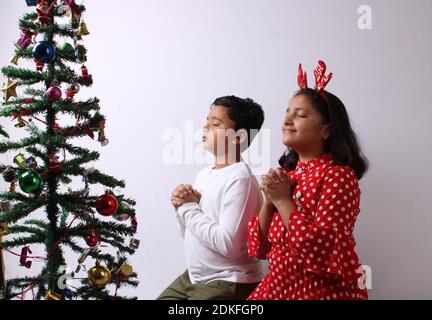 Zwei indische Kinder sitzen unter dem Weihnachtsbaum und machen einen Wunsch. Stockfoto