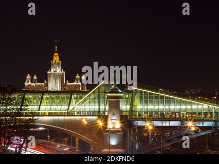 Lomonosov Moskauer Staatliche Universität bei wolkenloser Winternacht, im Vordergrund eine Fußgängerbrücke Bogdan Khmelnitsky über den Moskwa-Fluss, die bri Stockfoto