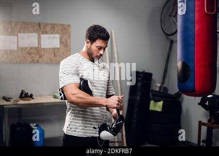 Ein junger Boxer bereitet sich auf das Training vor, zieht Boxhandschuhe im Fitnessstudio an Stockfoto