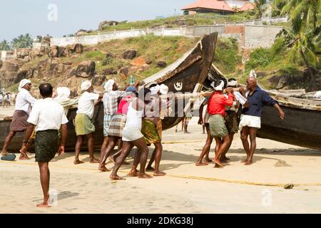 Kovalam, Kerala, INDIEN - JAN 15: Fischer schieben das Fischerboot am Strand aus dem Arabischen Meer am 15. JAN 2012 in Kovalam, Kerala, Indien. Stockfoto