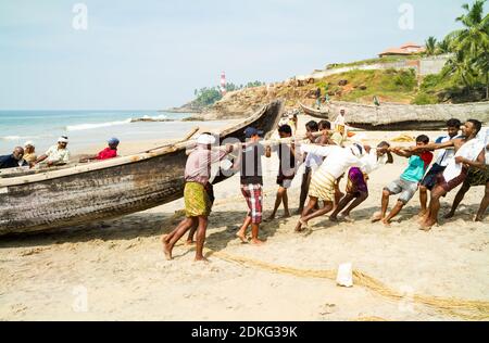 Kovalam, Kerala, INDIEN - JAN 15: Fischer schieben das Fischerboot am Strand aus dem Arabischen Meer am 15. JAN 2012 in Kovalam, Kerala, Indien. Stockfoto