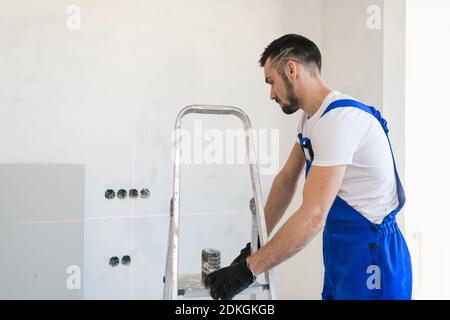 Ein bärtiger Baumeister bewegt eine Aluminium-Trittleiter um die Zimmer Stockfoto