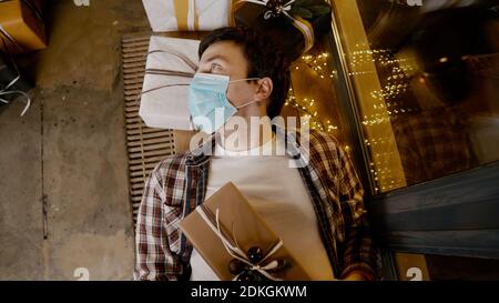 Depressiver Mann, Isolation zu Hause, Quarantäne COVID-19 Pandemie an Weihnachten. Pessimistischer Typ fühlt sich im hausdekorierten Neujahrsdekor auf Perio gefangen Stockfoto