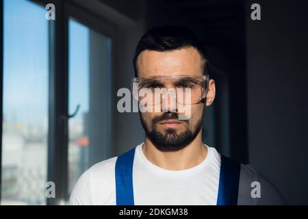 Junge Arbeiter in blauen Overalls und Kunststoff-Schutzbrille Stockfoto