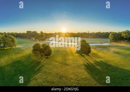 Wunderbarer Sonnenaufgang über dem Englischen Garten in München. Sonnenstrahlen leuchten durch die Bäume. Stockfoto