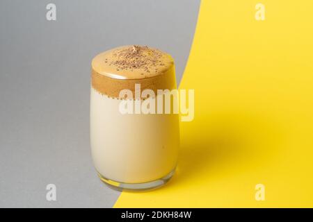 Dalgona Kaffee mit üppigem Schaum in einem Glas auf einem gelben und grauen Hintergrund. Trendige koreanische Getränk auf Trending Pantone Farben 2021 Stockfoto