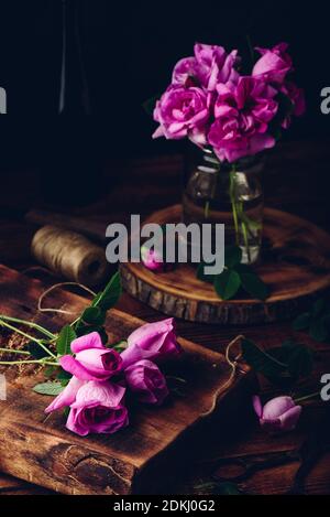 Rosa Gartenrosen auf rustikalem Holztisch und im Glas Mit Wasser Stockfoto