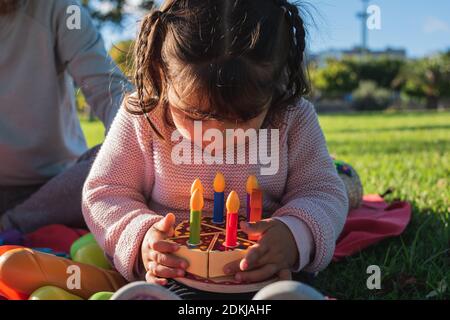 Kleines Mädchen mit einem Geburtstagskuchen in den Händen, die Kerzen ausblasen. Stockfoto