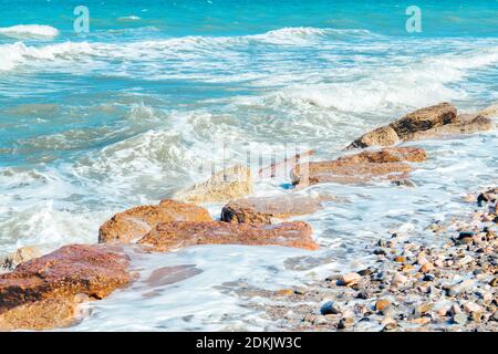 Oberfläche der Meereswellen während windigen Sommertag, Küste mit Kieselsteinen und cutwater. Stockfoto