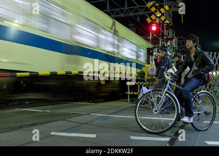 Ein Zug der Odakyu-Linie fährt durch einen Bahnübergang in der modischen Stadt Shimo Kitazawa, während die Menschen auf Fahrrädern und zu Fuß warten. Tokio, Japan Stockfoto