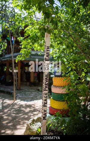 Peace Pole Botschaft neben bunten gestapelten Reifen und ein Baum Stockfoto