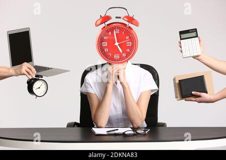 Junge Sekretärin mit Wecker statt Kopf und viel Arbeit am Tisch im Büro. Zeitmanagement-Konzept Stockfoto