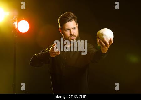 Männlicher Schauspieler mit menschlichem Schädel auf der Bühne Stockfoto