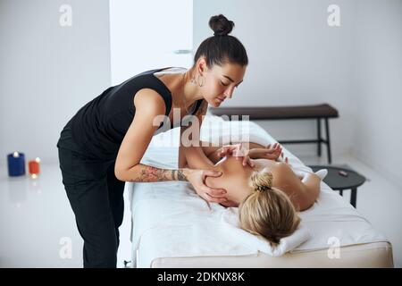 Frau in dunklen Kleidern, die mit Schulterpatient in der Massage arbeitet Schrank Stockfoto