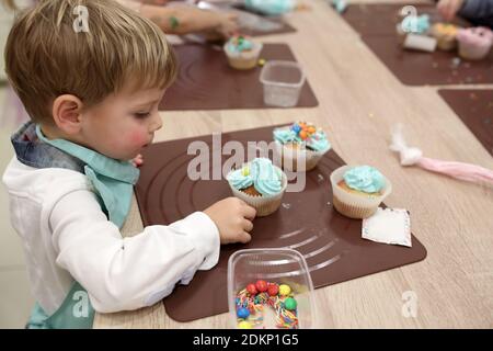 Boy schmückt die Muffins mit Streuseln in der Küche Stockfoto