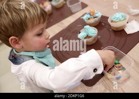 Kind schmückt die Muffins mit Streuseln in der Küche Stockfoto