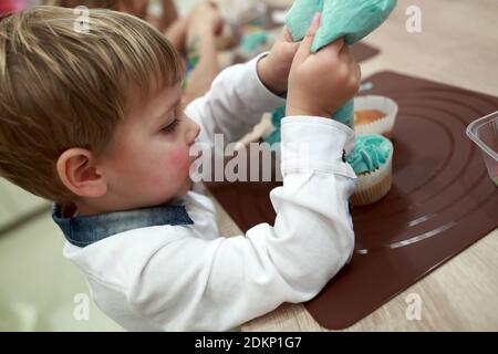 Kind schmückt Cupcakes mit Sahne in der Küche Stockfoto