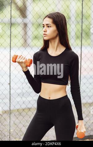 Schöne junge Frau führt Übungen mit Hanteln auf dem Spielplatz. Gesundes Lifestyle-Konzept. Stockfoto