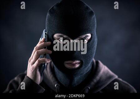 Criminal trägt schwarze Balaclava und Hoodie mit einem Smartphone in Die Dunkelheit Stockfoto