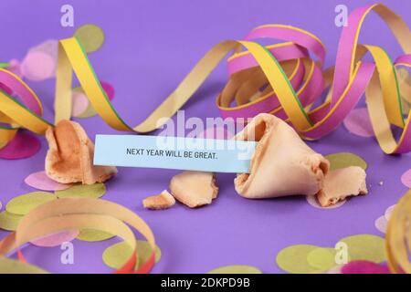 Optimistisches Silvester-Feierkonzept mit offenem Fortune Cookie Und Text "nächstes Jahr wird groß sein" im Hintergrund mit Papierstreamer Stockfoto