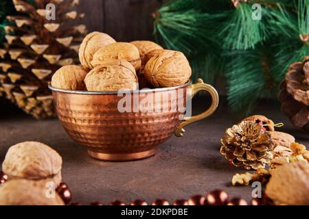 Walnüsse in einem Blechbecher, ganz und gehackt, neben der Füllung und Schalen. Präsentiert in einer Neujahrskomposition mit Tannenzapfen. Home Lagerung des Winters Stockfoto