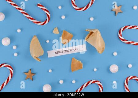 Weihnachtsgrüße mit offenem Glückskeks und Text 'Merry Christmas' auf blauem Hintergrund mit Zuckerstöcken, Sternen und Schneebällen Stockfoto