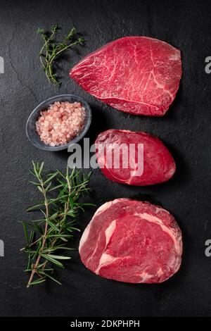 Fleischstücke, Topshot mit Salz und Rosmarin auf schwarzem Hintergrund Stockfoto