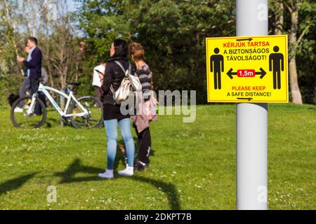 Please keep a safe distance covid-19 warning sign on post. People standing and watching in the background. Sopron, Hungary Stock Photo