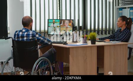 Gelähmte, unbewegte Freiberuflerin im Rollstuhl, die online mit Kollegen im Büro über Videomeeting diskutiert. Behinderter Geschäftsmann, der in einem Finanzunternehmen mit moderner Technologie arbeitet. Stockfoto