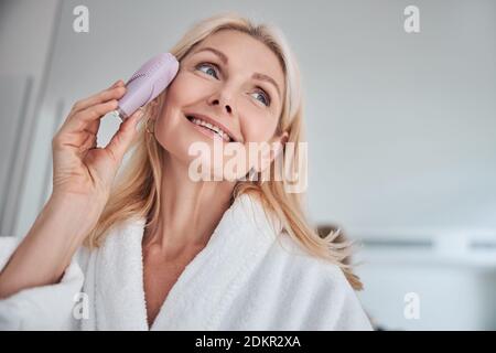 Schöne Frau genießen tolle Zeit während der Massage auf der Haut Gesicht mit elektrischem Massagegerät für die Gesichtsbürste Stockfoto